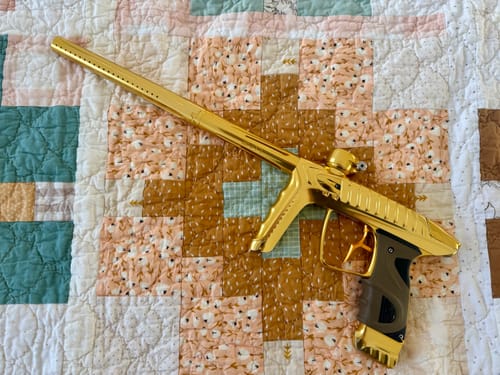 Customer's shiny gold Luxe TM40 paintball marker with the Nighthawk trigger installed, resting on a quilt.