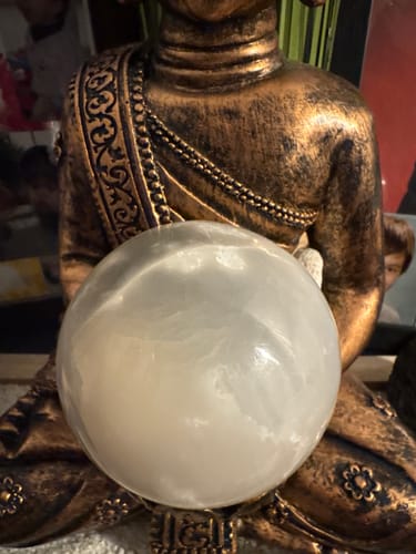 Photo d'un client montrant la sphère en Sélénite lumineuse, tenue dans les mains d'une statue de Bouddha.