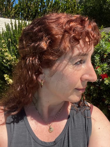 Reviewer outdoors wearing the gold Waikiki Shell Necklace against a background of green foliage.