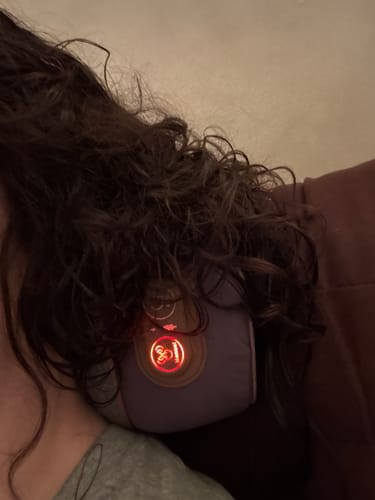 Reviewer using the heat setting on their purple Callixe Thera Pillow. The device is on their neck with the control panel lit red.