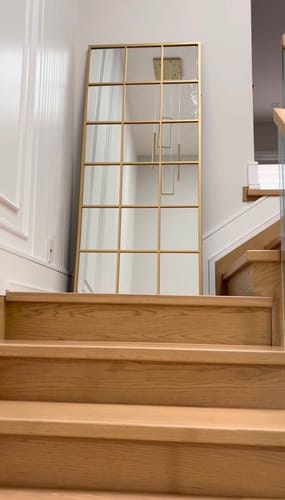 Customer's Modern Gold Grid Wall Mirror leaning against a white wall at the top of a wooden staircase.