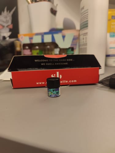Customer's small vial of Glasswater scent with a colorful label, shown on a desk in front of its packaging.