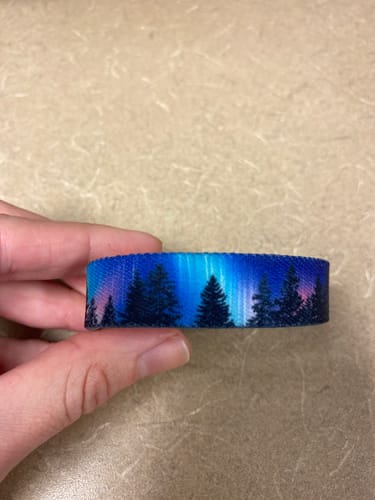 Customer's hand holding the Follow Your Dreams Bracelet, showing the colorful Northern Lights and tree design.