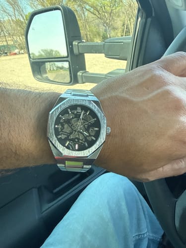 A reviewer's wrist wearing the silver Lucky Fours® Spine watch, showing its skeleton face, while inside a vehicle.