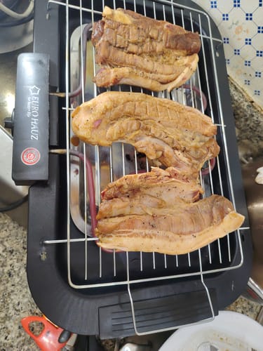 Customer grilling three large pieces of pork on the black Eurohauz Smokeless Grill.