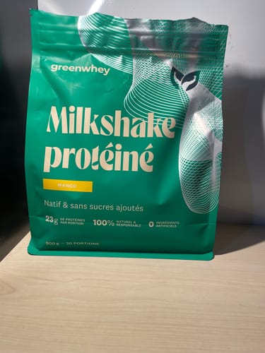 Photo d'un client montrant le sachet vert du Milkshake Protéiné saveur mangue sur une table.