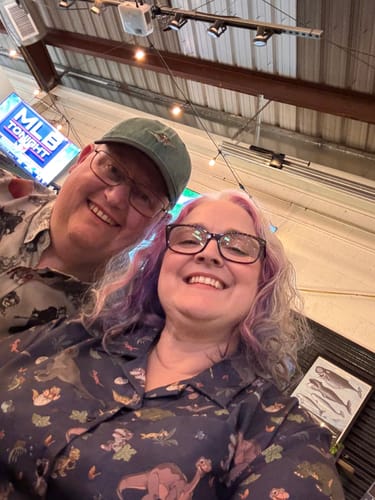 Reviewer smiling in a selfie, wearing the blue "Prehistoric Pals" shirt with its dinosaur pattern.