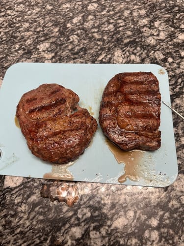 Customer's two grilled steaks from the Classic Cuts Collection resting on a light blue cutting board.