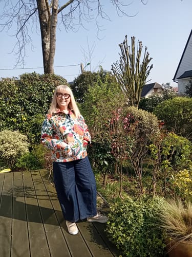 Cliente portant la veste Solveig jacquard floral avec un jean large sur une terrasse en bois.