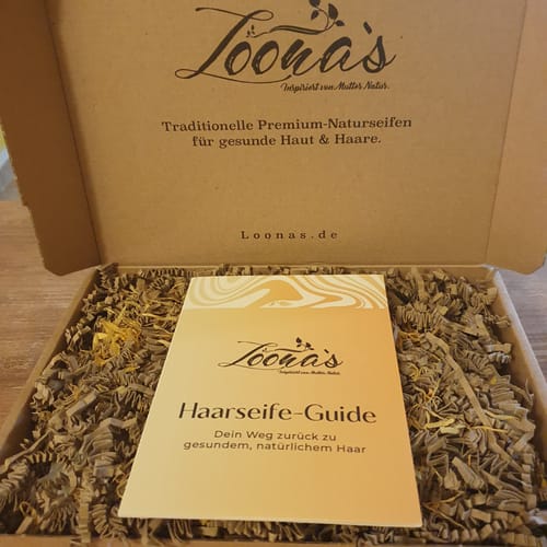 Kundenrezension: Geöffnete Loona's Box mit Haarseife-Guide auf Füllmaterial.