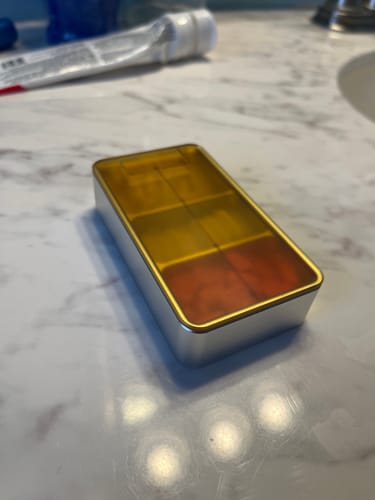 Customer's Ultem Lid with Metal Base pill case resting on a white marble countertop.