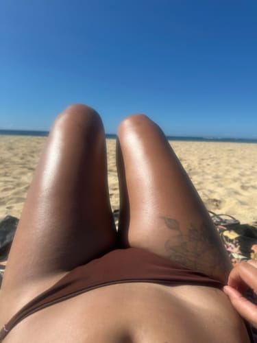 Reviewer's perspective of their glowing, tanned legs at the beach after using SPF 15 Protective Tanning Oil.