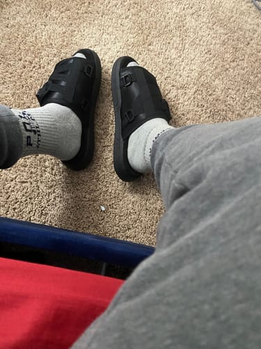 Customer's top-down view of their feet in black Mystery DracoSlides, worn with grey socks on a carpet.