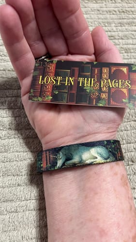 Customer wearing the unicorn version of the Lost In The Pages Bracelet on their wrist, holding the product tag.