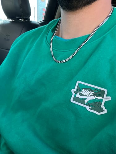 Primer plano de un cliente que lleva la Cadena Miami Cuban de 5 mm sobre una sudadera verde.