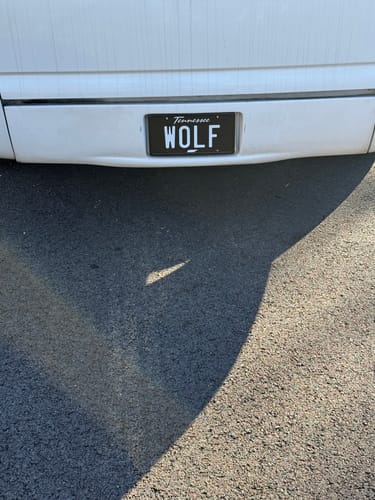 Reviewer's Tennessee Blackout Metal License Plate, customized with 'WOLF', mounted on a white car.