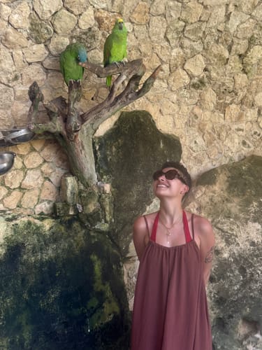 Customer smiling and wearing a cross pendant necklace in an outdoor setting with two parrots.