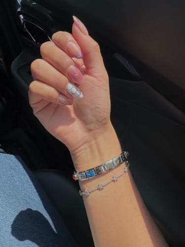 Cliente luciendo en su muñeca una pulsera italiana con varios charms brillantes junto a otra pulsera delgada.