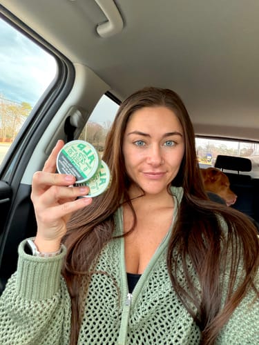 Reviewer in a car holding two tins of Tropical Fruit Nicotine Pouches.