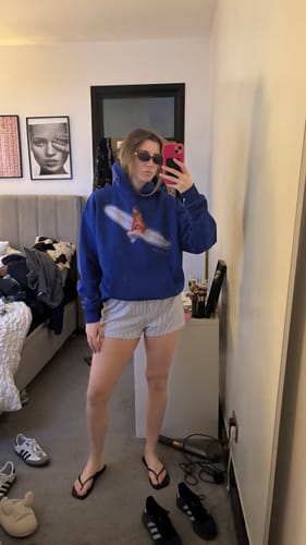 Reviewer taking a mirror selfie wearing the oversized surf's up blue hoodie with shorts.