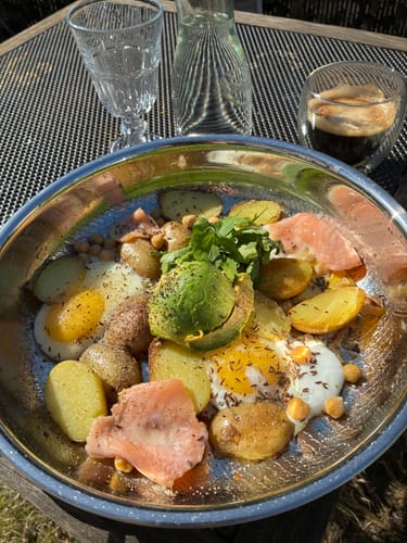 Rezensent zeigt sein Frühstück aus Eiern und Kartoffeln in einer glänzenden Titanschale.