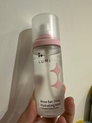 Customer holding the frosted bottle of Rose Set Glow Hydrating Mist, showing its clear liquid and pink details.