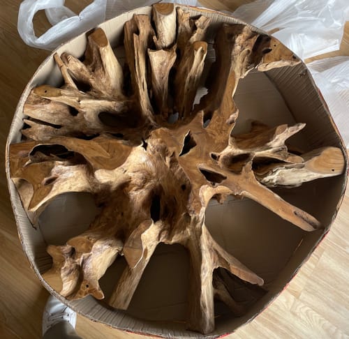 Ein Kunde zeigt die ausgepackte Teakholzwurzel des Couchtischs NAGA in der runden Verpackung.