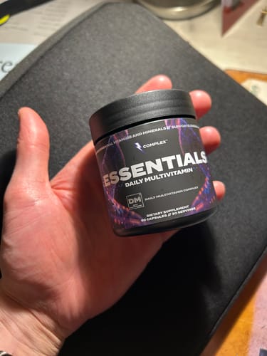 Customer holding the black tub of Complex Essentials Multivitamin in their hand.
