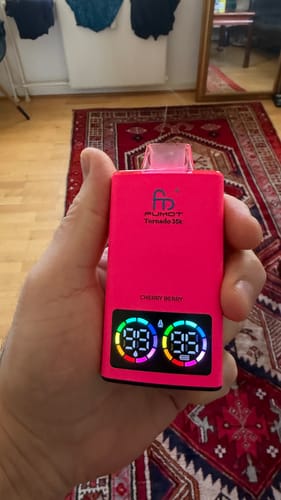 Reviewer holding a pink RandM Tornado vape, showing its digital display with battery and liquid levels at 99.
