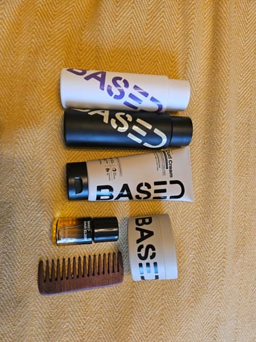 Customer's Based Curl Cream shown with other hair products and a comb on a yellow surface.