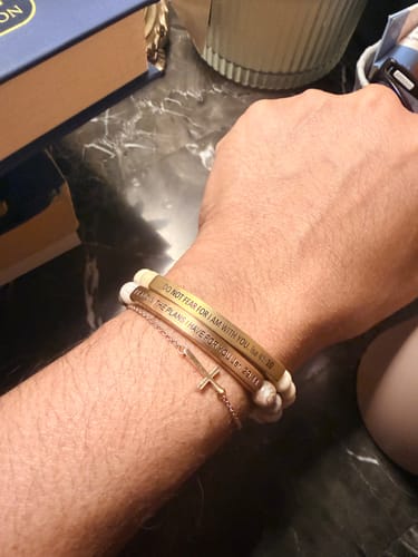Reviewer wearing the engraved 'DO NOT FEAR' cuff, stacked with another verse bracelet and a cross chain on their arm.