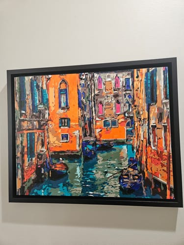 Reviewer's finished Venice Canals paint-by-numbers kit, featuring colorful buildings and framed on a wall.