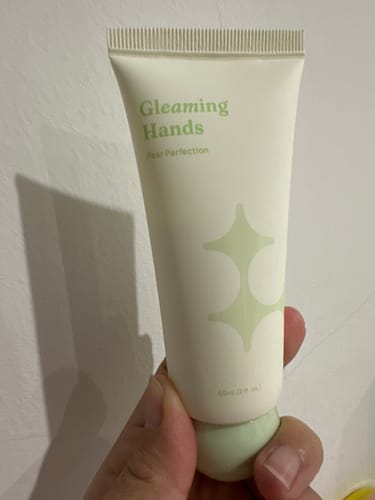 A reviewer's hand holding the pale green tube of Gleaming Hands Pear Perfection cream.