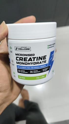 Customer holding a white tub of Wellcore Micronised Creatine Monohydrate in the Kiwi Kick flavor.