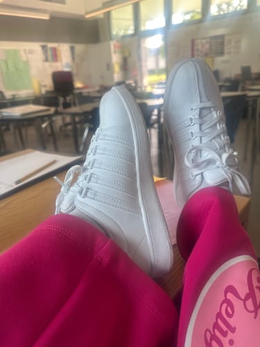 Reviewer's white Classic VN shoes propped on a desk, paired with bright pink leggings in a classroom setting.