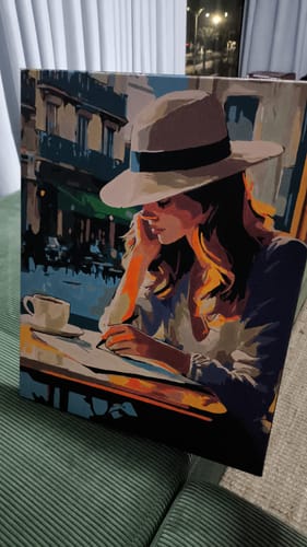 לקוחה מציגה ציור גמור של ערכת הצביעה לפי מספרים שלה, המתאר אישה עם כובע בבית קפה.