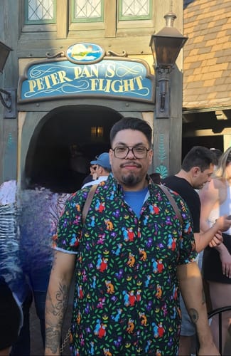 Reviewer wearing the colorful Peter Pan "Never Grow Up" shirt in front of the Peter Pan's Flight ride.