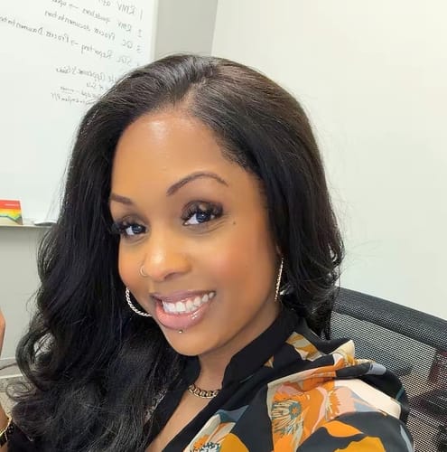 Reviewer smiling in a long, dark Sensationnel Bare Lace wig, showing its natural hairline and curly style.