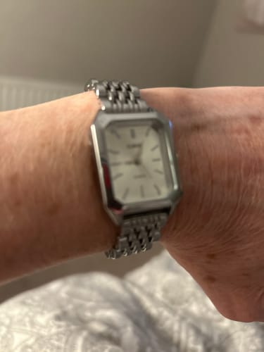Customer's wrist showing the silver CLAIRE DE MAINS watch with its link bracelet and rectangular white face.