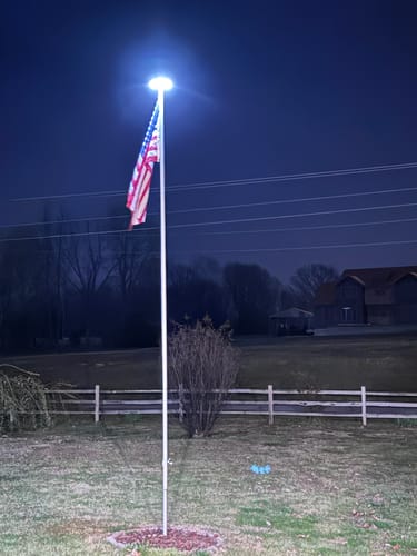 Customer's Silver Solar Flagpole Top Light brightly illuminating an American flag at night in a yard.