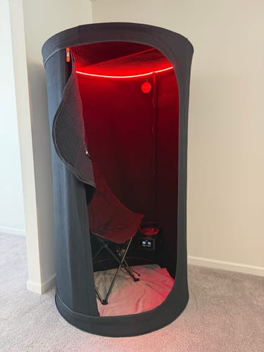 Customer's Sauna Pod 2.0 set up in a room with the door open, revealing a chair inside under red LED lighting.