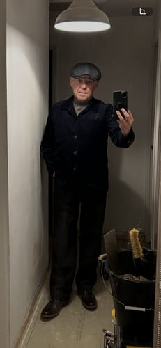 Reviewer taking a mirror selfie while wearing the dark Indigo Corduroy Chore Coat and a flat cap.
