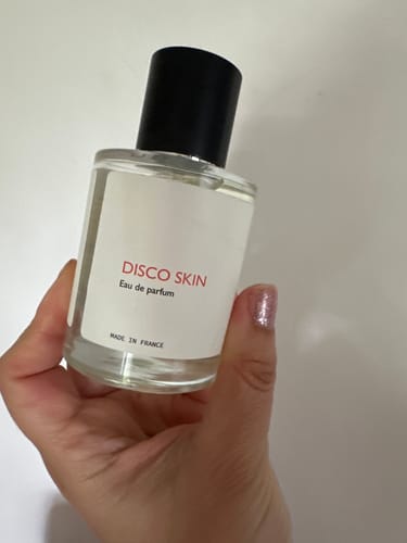 Reviewer holding the clear Disco Skin eau de parfum bottle with a black cap.