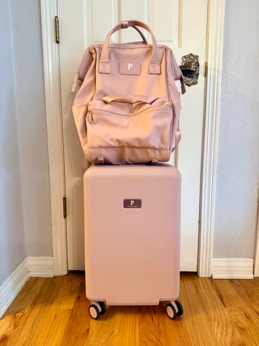 Reviewer's blush Cascade Backpack sitting on top of a matching suitcase in a hallway.