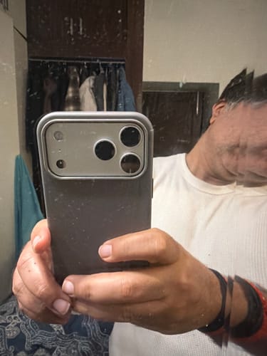 A reviewer's mirror selfie showing the graphite grey Signature Leather Magsafe Case on an iPhone held in hand.