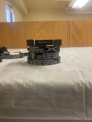 Customer's stack of black customized memorial bracelets showing personalized text and Army logos on a table.