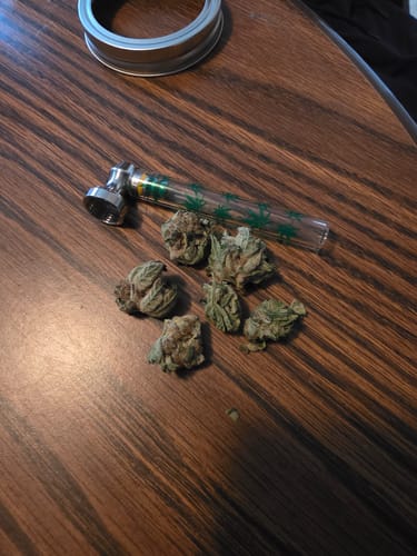 Customer's Purple Punch dried buds on a wooden table next to a glass pipe.