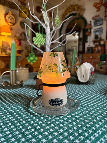 Reviewer's Lemon Macaroon candle shown lit on a table with a decorative, orange jar shade painted with green shamrocks.