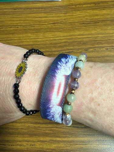 Customer's wrist wearing the My Angel Bracelet stacked with a patterned watch band and a sunflower bracelet.