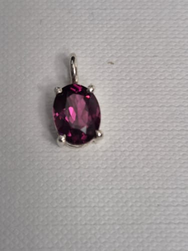 Photo d'un client montrant le pendentif Grenat Rhodolite ovale sur un tissu blanc. La pierre est brillante et de couleur rose.